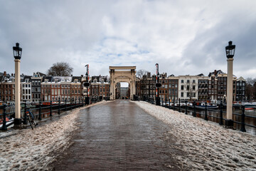 Fototapeta premium Narrow historic bridge, lit at night, crosses the river Amstel in Amsterdam