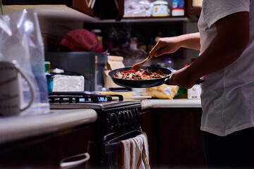 Young man preparing food in shop. Cooking meat with vegetables. frying meat with red peppers, tomato and onion in a frying pan.