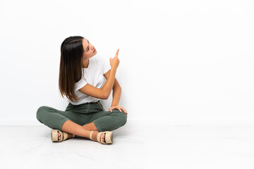 Teenager girl sitting on the floor pointing back with the index finger