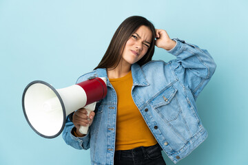 Teenager girl isolated on yellow background holding a megaphone and having doubts