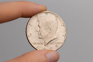 A hand holds a coin of 50 american cents with a portrait of John F. Kennedy on a white background close-up - obrazy, fototapety, plakaty