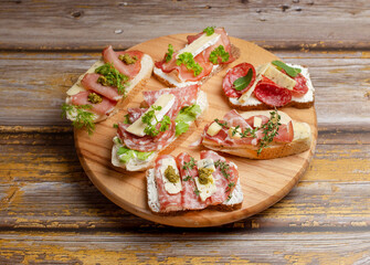 Open sandwiches with prosciutto,, cream, blue cheese, salami and herbs on cutting board, close up