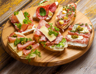 Delicious appetizer bruschetta with bacon, blue cheese, herbs and prosciutto on table, close-up