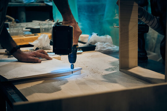 Hands Of Man Drilling Holes In Plywood And Woman Assembling Desk Drawer. People Works At Carpentry Workshop. Small Business Enterprise For Furniture Production And Restoration. Carpenter Workshop