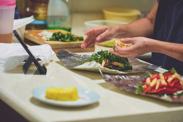 Homemade vegan food. Salmon with spinach, tomato, onion, red pepper, olive oil, potato, pineapple. Healthy breakfast. Natural food. Woman preparing food following a recipe on her cell phone.