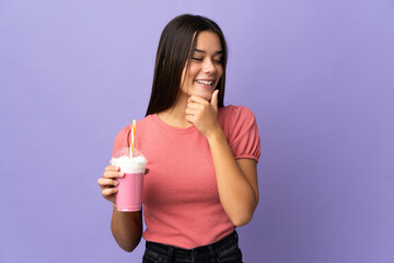 Teenager girl holding a strawberry milkshake looking to the side and smiling