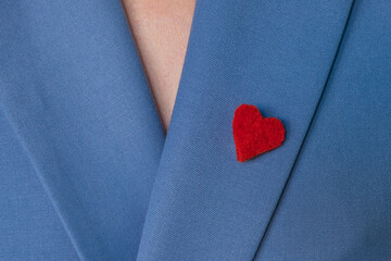 Beautiful brooch in the form of a red heart made of felt on the lapel of a bright blue jacket. Symbol of the holiday Valentine's Day. Beautiful clothing details - obrazy, fototapety, plakaty