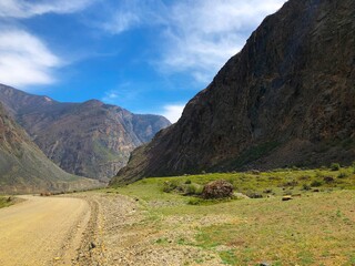 A road without asphalt, a primer among the mountains in spring and a blue sky with clouds