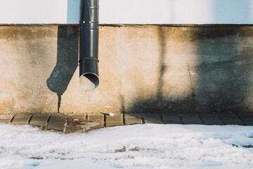 Photo of a downpipe in winter with frozen water.
