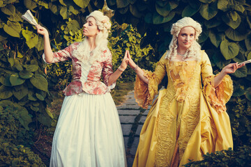 Fototapeta premium Portrait of two blonde woman dressed in historical Baroque clothes with old fashion hairstyle, outdoors. Luxurious medieval dress