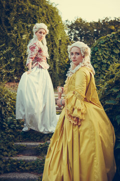 Portrait of two blonde woman dressed in historical Baroque clothes with old fashion hairstyle, outdoors. Luxurious medieval dress