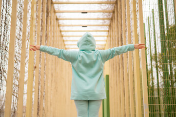 Caucasian woman spreading her arms in a mint hoodie walks alone in the park.