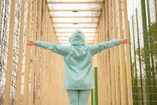Caucasian woman spreading her arms in a mint hoodie walks alone in the park.