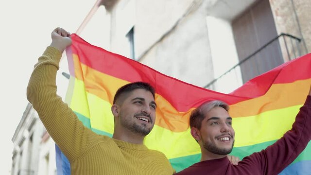 Gay male couple holding rainbow flag at Lgbt pride parade - Equality human rights concept