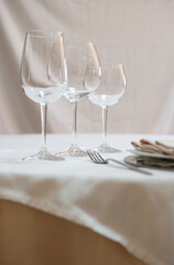 A dining table set for eating. Wine glass, water glass, plate, fork, knife, napkin, tablecloth.