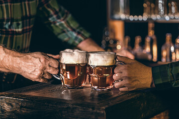 Man's hands clinking beer mugs on bar counter in a restaurant, pub. Drinks, ale, cider, malt beverage at bar. Selected focus, shallow depth of field