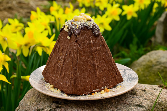 Cottage cheese chocolate Easter with a pattern in the form of a cross on a background of yellow flowers of daffodils. Spring greeting card. The concept of the holiday. Easter dish.