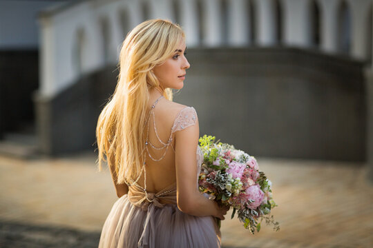 Portrait of an elegant pretty woman wearing grey wedding dress and posing in the street. Bride holds a bouquet of pastel flowers and greenery