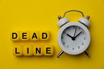Deadline word on plastic cubes with analog alarm clock isolated on yellow background. Concept of self warning to get job done ontime in very tight deadline to meet expectation. Business concept.
