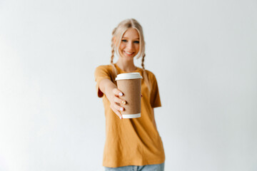 Happy blonde woman with plaits smiling, offering takeaway coffee. The work of barista