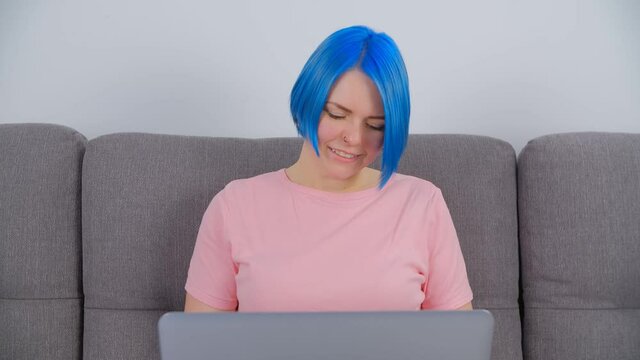 Creative white woman with dyed blue hair working on laptop at home. Studen female learning online with modern computer. Freelancer person doing distant work on notebook pc connected to internet
