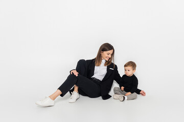stylish and cheerful woman sitting near toddler son on grey.