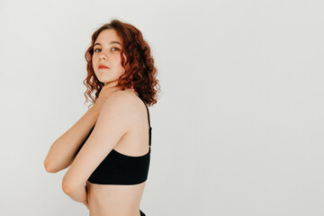 Young sensual woman with curly hair looking at the camera, holding herself with her arms, standing over white background