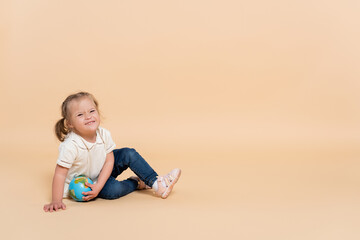 happy kid with down syndrome sitting with small globe on beige.