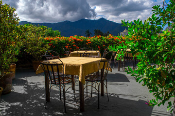 tables on an outdoor terrace overlooking the mountainous natural landscape, a cloudy sky and a volcano.