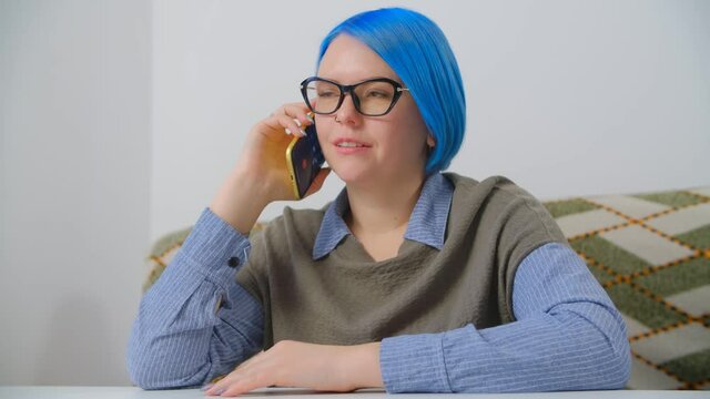 Young woman with dyed blue hair talking on phone. 4k stock video of white nerd female calling on smartphone