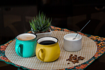 Coffee moment in company. Different colored cups with black coffee and latte on a table with coffee beans, a jug of milk and a container with sugar.