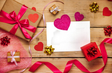 Top view photo of Valentine's day decor gift box, paper heart, a sheet of paper on a wooden background.