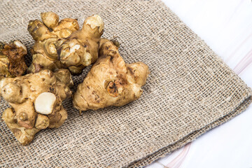 The jerusalem artichoke tuber lies on a napkin made of natural fabric on a light table.