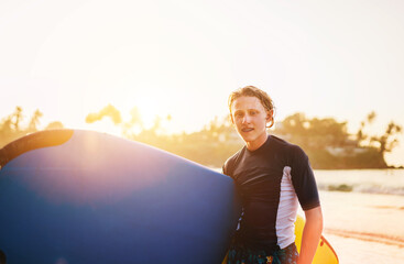 Portrait of a teen boy with Dental braces with surfboard goes for surfing. He is smiling and walking into the water. Happy childhood and active vacation time concept.