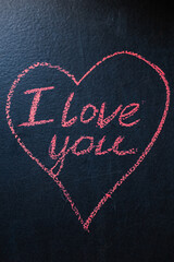 A heart is drawn in pink chalk on a dark board and "I love you" is written. The Valentine's Day card is vertical.