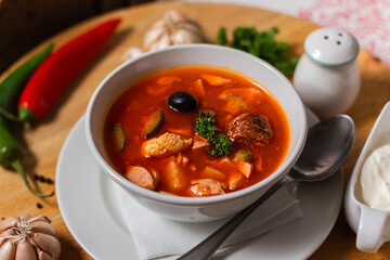 solyanka national team. a portion of spicy red hot soup with tomatoes, sausages and olives on a wooden background