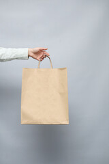 Female hand hold brown blank paper bag on grey background