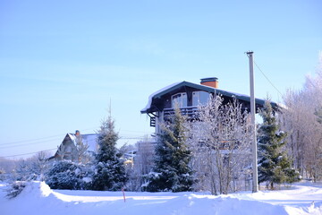 A house in the mountains is snow-covered in winter, and there are three Christmas trees nearby
