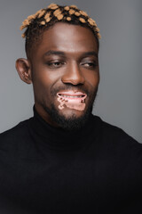 joyful african american man with vitiligo skin, wearing black turtleneck isolated on grey.