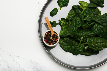 Organic food concept with spinach leaves on a plate with pepper top view closeup. White background