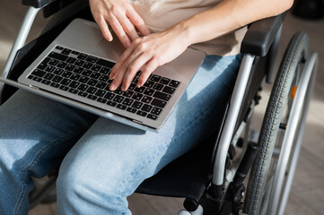 Caucasian woman in a wheelchair typing with a laptop from home. Remote work for people with disabilities.