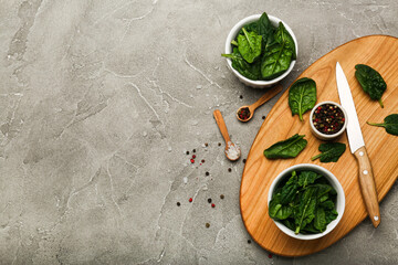 spinach leaves in a bowl on a wooden cutting board and with wooden spoons with salt and pepper. Gray background, top view