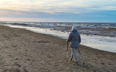 A woman in age is nordic walking next to the sea in winter time.