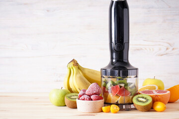 Hand blender and accessories with sliced fruit on a wooden background, place for text. Close up..