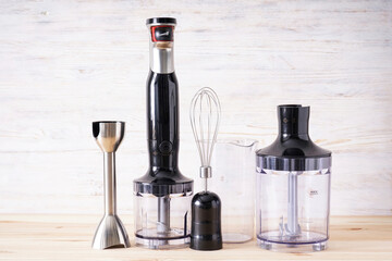 Black plastic electrical hand blender and accessory on the wooden background.