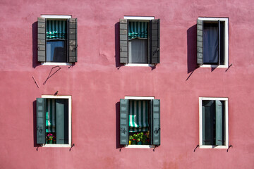 Fototapeta na wymiar six shuttered venetian windows on a canal side building with bright pink paintwork