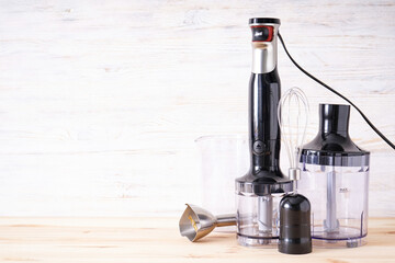 Black plastic electrical hand blender with stainless steel body and accessory on the wooden background, place for text.