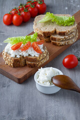 Fototapeta na wymiar Slices of rye bread with cottage cheese and tomatoes on wooden plate on grey background