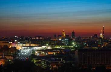 Red and blue saturated sunset with light clouds in the city. Silhouette of town and lights of railway station and railroad. Moscow, Russia.