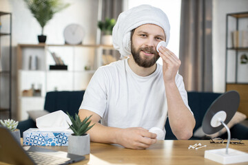 Bearded, stylish young Caucasian man in towel on his head performs hygienic procedures for cleaning...